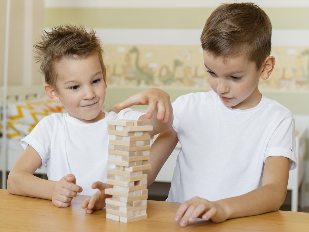 Deux enfants qui collaborent pour bâtir une tour, développant des compétences sociales importantes.